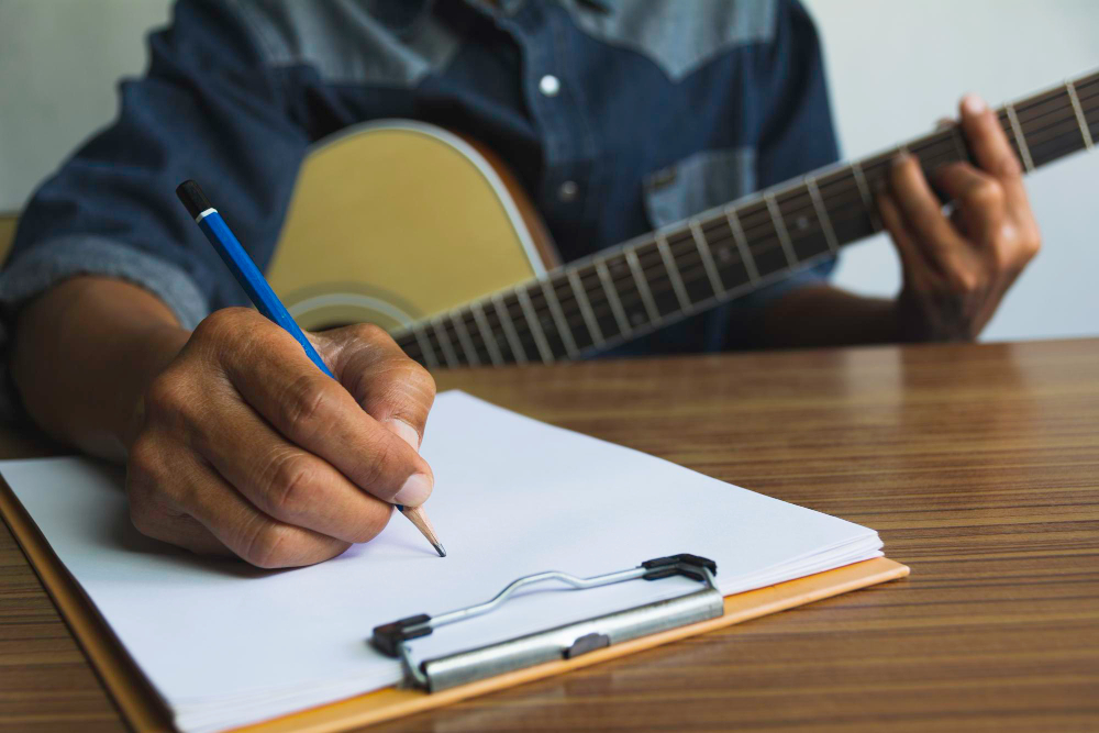 Músico tocando violão enquanto faz anotações em papel sobre a mesa, representando a relação entre carreira artística e suporte jurídico contratual. 